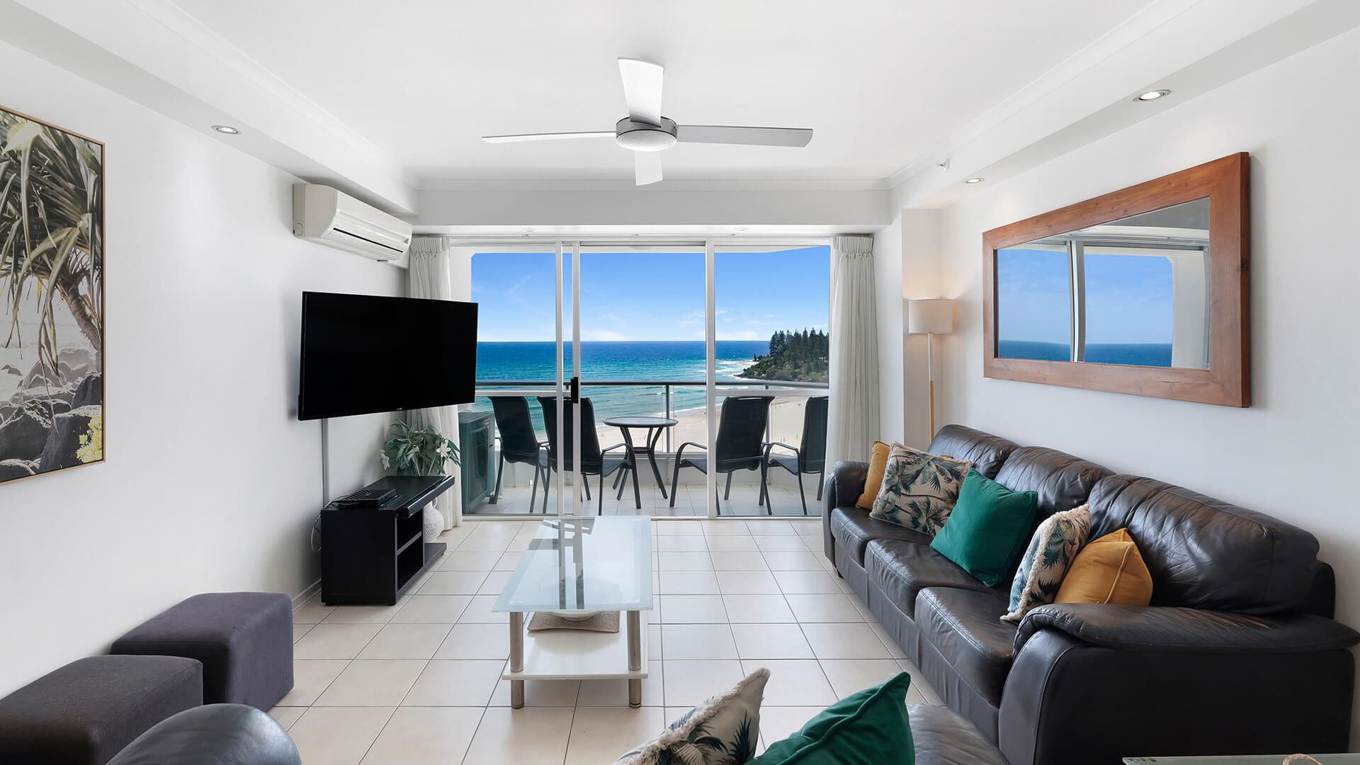 Living room in the 2 Bedroom Superior Ocean View Apartment with leather sofas, tropical cushions, wall-mounted TV and ocean-view balcony.
