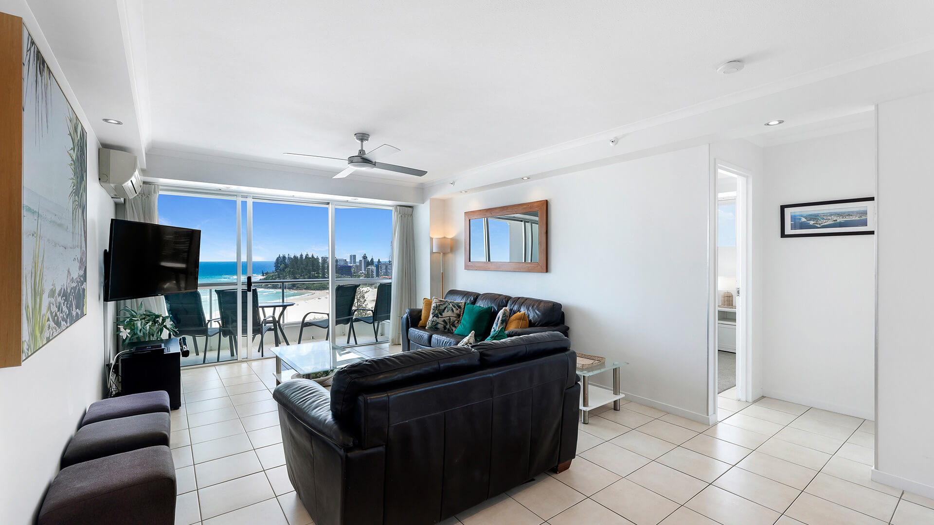Coastal living area in the 2 Bedroom Superior Ocean View Apartment with leather sofas, tiled floors, balcony access with ocean and beach views.