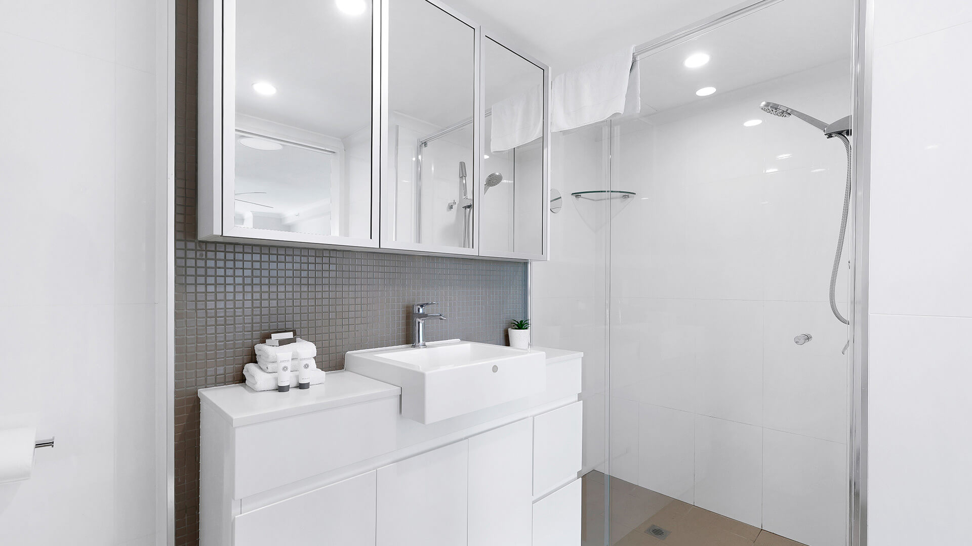 Modern bathroom in the 2 Bedroom Superior Ocean View Apartment featuring a glass shower, large vanity, mirrored cabinets, and bright lighting.