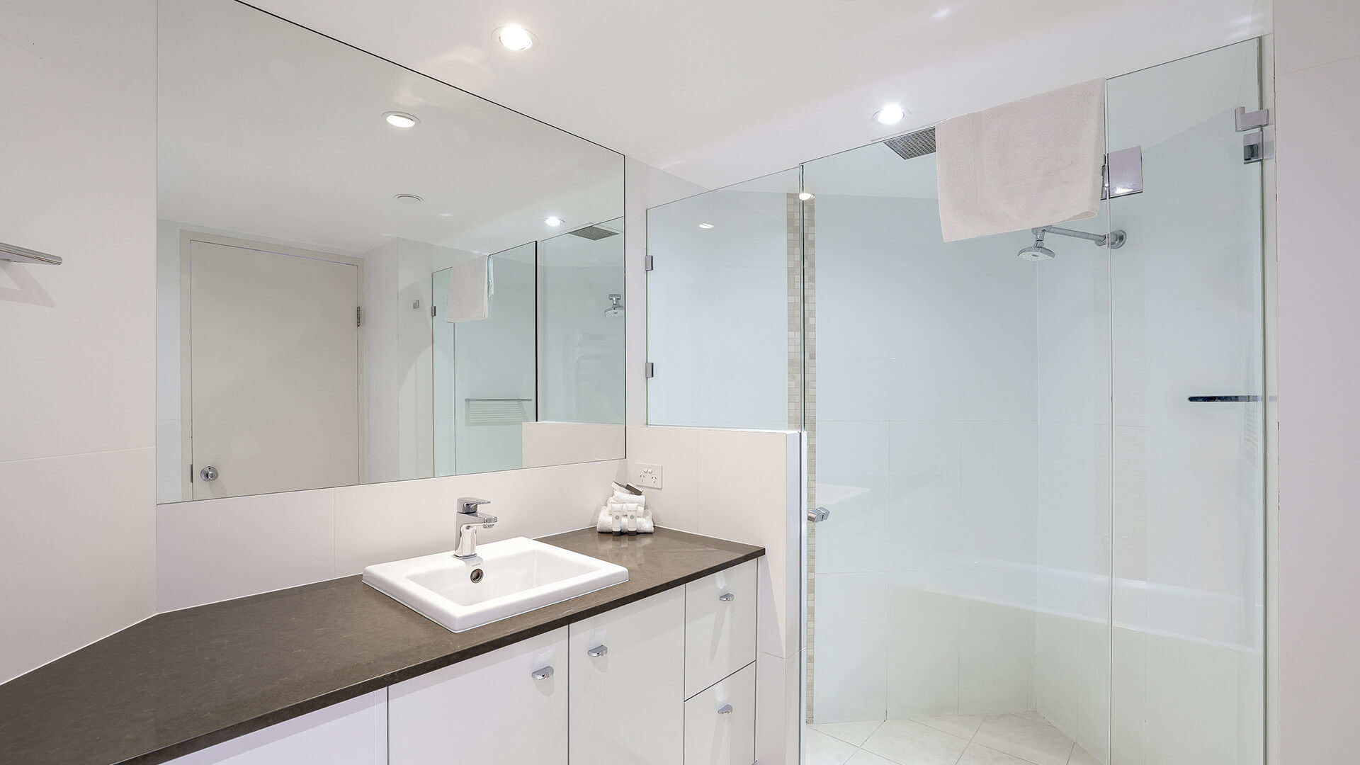 Modern bathroom in the Superior 3 Bedroom Ocean View Apartment featuring a large vanity, wide mirror, and glass-enclosed shower.