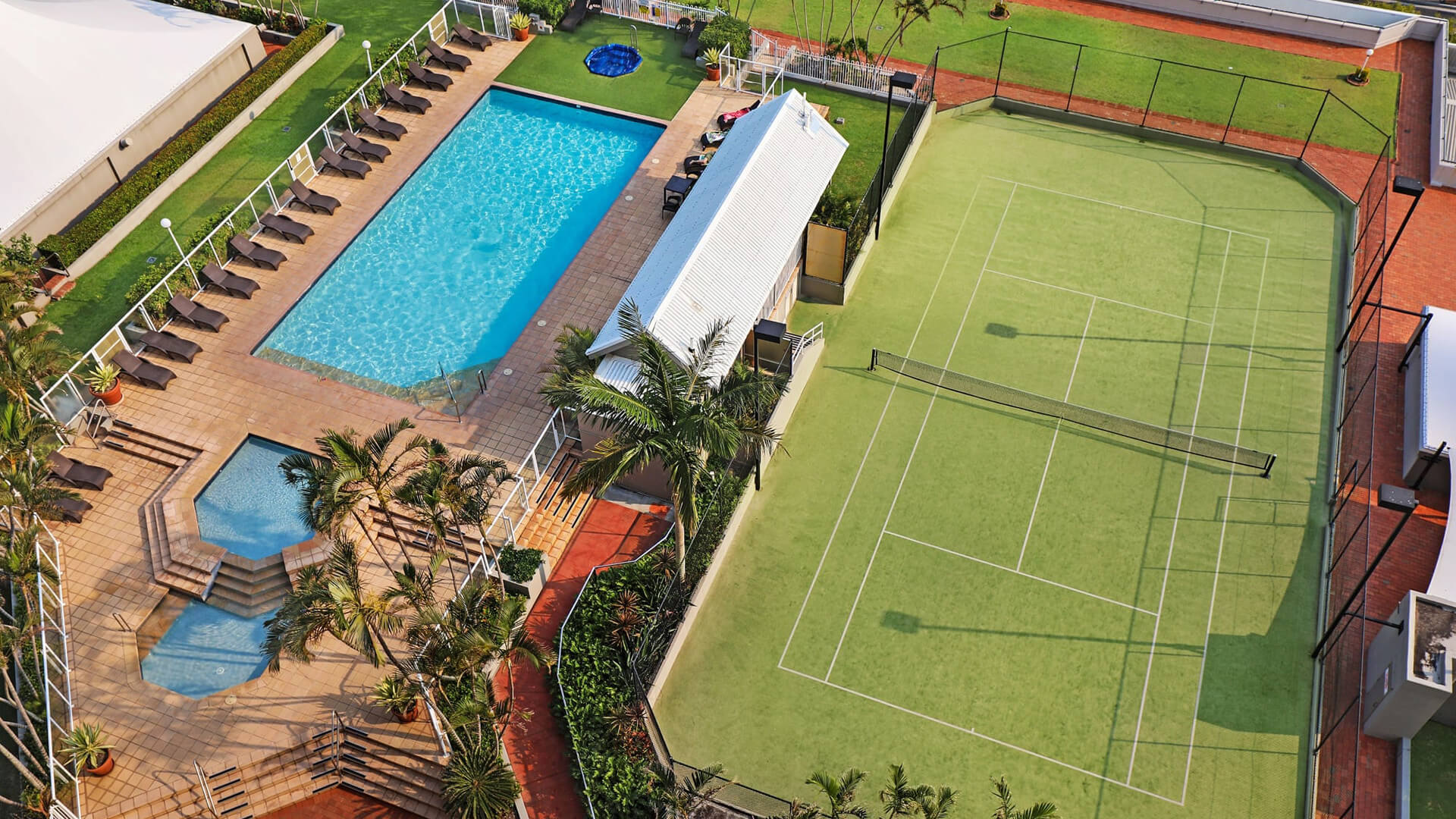 ULTIQA Points North. Arial View of Swimming Pools, Deck, Seating Areas and Tennis Court.