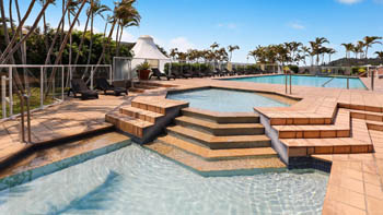 Outdoor tiered swimming pool area at ULTIQA Points North with sun loungers, palm trees, and clear blue skies.