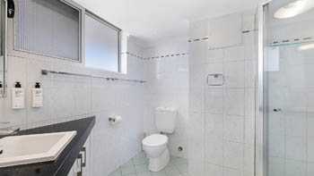 Bathroom in a 2 Bedroom Superior Ocean View Apartment with glass-enclosed shower, white vanity, toilet & frosted windows providing natural light.