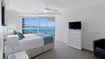 Master bedroom in the 2 Bedroom Superior Ocean View Apartment with a queen bed, dresser with TV, and large windows overlooking the ocean.