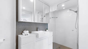 Modern bathroom in the 2 Bedroom Superior Ocean View Apartment featuring a glass shower, large vanity, mirrored cabinets, and bright lighting.