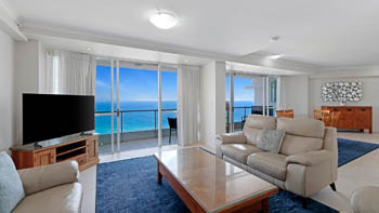 Spacious living area in a Superior 3 Bedroom Ocean View Apartment with leather sofas, glass coffee table & balcony with sweeping ocean views.