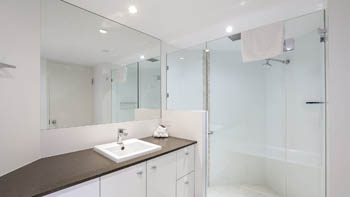 Modern bathroom in the Superior 3 Bedroom Ocean View Apartment featuring a large vanity, wide mirror, and glass-enclosed shower.