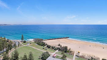 Expansive beach and ocean view featuring golden sand, turquoise water, and a grassy park area along the coastline.