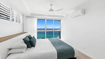 Main bedroom in the Deluxe 3 Bedroom Ocean View Apartment, featuring a king bed, coastal décor, & panoramic ocean views from floor-to-ceiling windows.