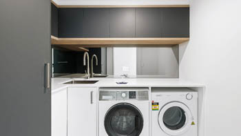 Internal laundry in the Deluxe 3 Bedroom Ocean View Apartment at ULTIQA Points North, featuring a washer, dryer, sink, and contemporary cabinetry.
