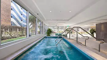 Indoor spa with bubbling jets at ULTIQA Beach Haven on Broadbeach, featuring floor-to-ceiling windows, stainless steel handrails and poolside lounge seating for ultimate relaxation.