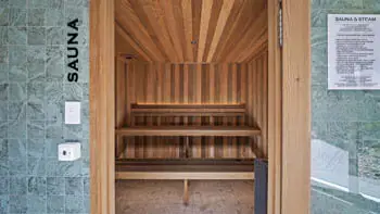 Modern cedar-lined sauna at ULTIQA Beach Haven on Broadbeach, featuring tiered bench seating, tiled entrance wall and wellness guidelines for a rejuvenating relaxation experience.