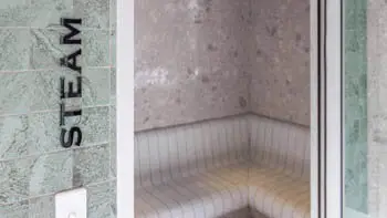 Modern tiled steam room at ULTIQA Beach Haven on Broadbeach, featuring curved seating and soft lighting for a tranquil wellness experience.