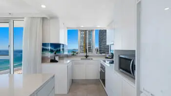 Contemporary kitchen featuring sleek white cabinetry, modern appliances, and city views framed by floor-to-ceiling windows.