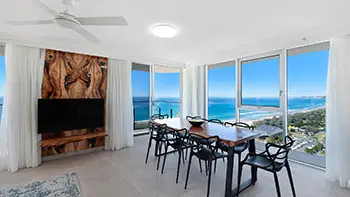 Dining featuring a wooden dining table, modern black chairs, and panoramic views of the Gold Coast coastline through floor-to-ceiling windows.