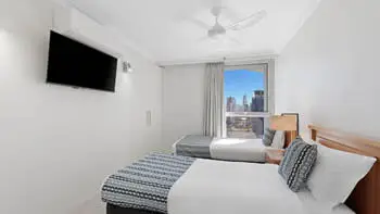 Second bedroom in the 2 Bedroom Ocean View Apartment at ULTIQA Beach Haven on Broadbeach with two single beds, TV, and city views.
