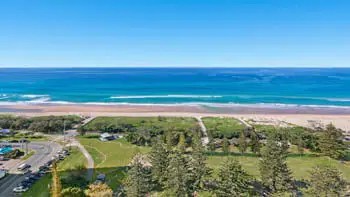 Aerial view of parklands and pathways leading to the beach, with clear blue skies and waves rolling onto the sand, seen from the 2 Bedroom Ocean View Apartment at ULTIQA Beach Haven on Broadbeach.