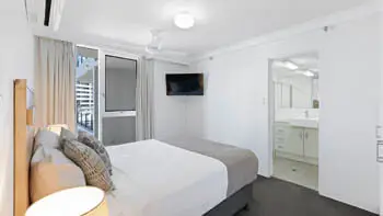 Master bedroom at ULTIQA Beach Haven on Broadbeach featuring a king bed, flat-screen TV, air conditioning, and direct access to a private ensuite.