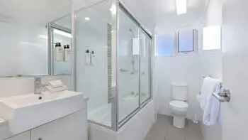 Bright bathroom at ULTIQA Beach Haven on Broadbeach featuring a shower-over-bath, modern vanity, toilet, and complimentary amenities.
