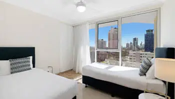 Second bedroom in the Standard 2 Bedroom Ocean View Apartment at ULTIQA Beach Haven on Broadbeach featuring a queen and single bed with city views.