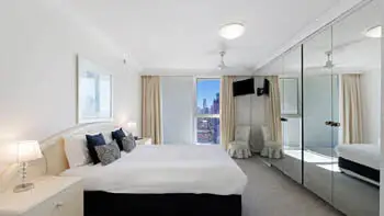 Main bedroom in the Standard 2 Bedroom Ocean View Apartment at ULTIQA Beach Haven on Broadbeach, featuring a king bed, mirrored wardrobes, and city skyline views.