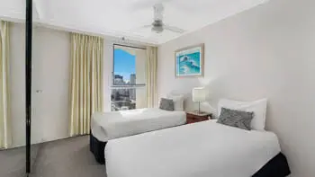 Second bedroom in the Standard 2 Bedroom Ocean View Apartment at ULTIQA Beach Haven on Broadbeach, featuring two single beds and city views.