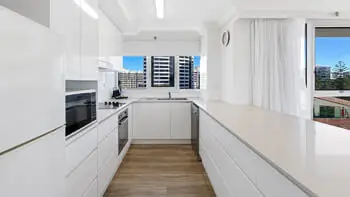 Modern kitchen in the Standard 2 Bedroom Ocean View Apartment at ULTIQA Beach Haven on Broadbeach, featuring sleek white cabinetry, full-size appliances, and city views through large windows.