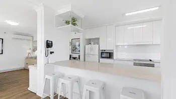 Spacious kitchen with white cabinetry, full-size fridge, and breakfast bar seating in the Standard 2 Bedroom Ocean View Apartment at ULTIQA Beach Haven on Broadbeach.
