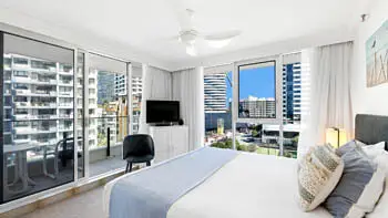 Master bedroom in the Standard 2 Bedroom Ocean View Apartment at ULTIQA Beach Haven on Broadbeach, featuring a comfortable bed, ceiling fan, and large windows with city views.