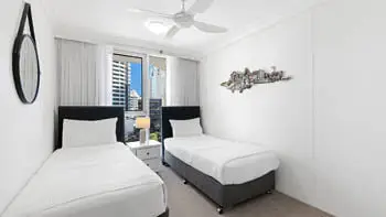 Second bedroom in the Standard 2 Bedroom Ocean View Apartment at ULTIQA Beach Haven on Broadbeach, featuring two single beds, ceiling fan, and city views.