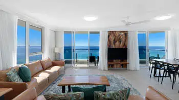 Spacious oceanfront living area with leather lounges, coastal décor, dining area, and floor-to-ceiling doors to uninterrupted beach views.