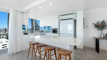 Modern kitchen in the Premium 2 Bedroom Ocean View Apartment at ULTIQA Beach Haven on Broadbeach with island bench, timber stools, and skyline views.
