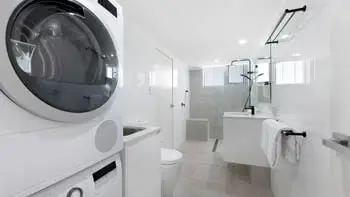 Modern bathroom and laundry combination, featuring a washer, dryer, walk-in shower, and vanity.