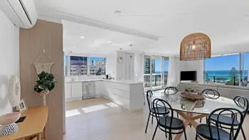 Open-plan kitchen, dining, and living featuring modern coastal décor, full kitchen, and balcony with stunning ocean views.