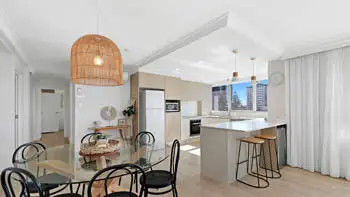 Bright open-plan dining and kitchen featuring coastal décor, modern appliances, breakfast island, and city views through large windows.