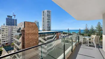 Spacious balcony featuring ocean views, an outdoor dining table, and a glass balustrade overlooking the pool and Broadbeach skyline.