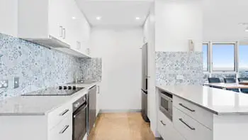 Modern white kitchen with a blue tile backsplash. Fully equipped with oven, stove, microwave and a lot of storage at ULTIQA Beach Haven on Broadbeach.