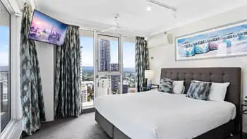 Master bedroom with dark headrest, whit plush bedding and a view of the Gold Coast at ULTIQA Beach Haven on Broadbeach.