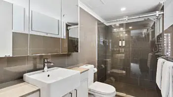 Bathroom with stone tiles, white sink, toilet and a walk-in shower at ULTIQA Beach Haven on Broadbeach.