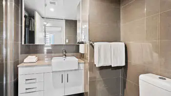 Second bathroom with clean white towels, sink and a toilet in modern style at ULTIQA Beach Haven on Broadbeach.