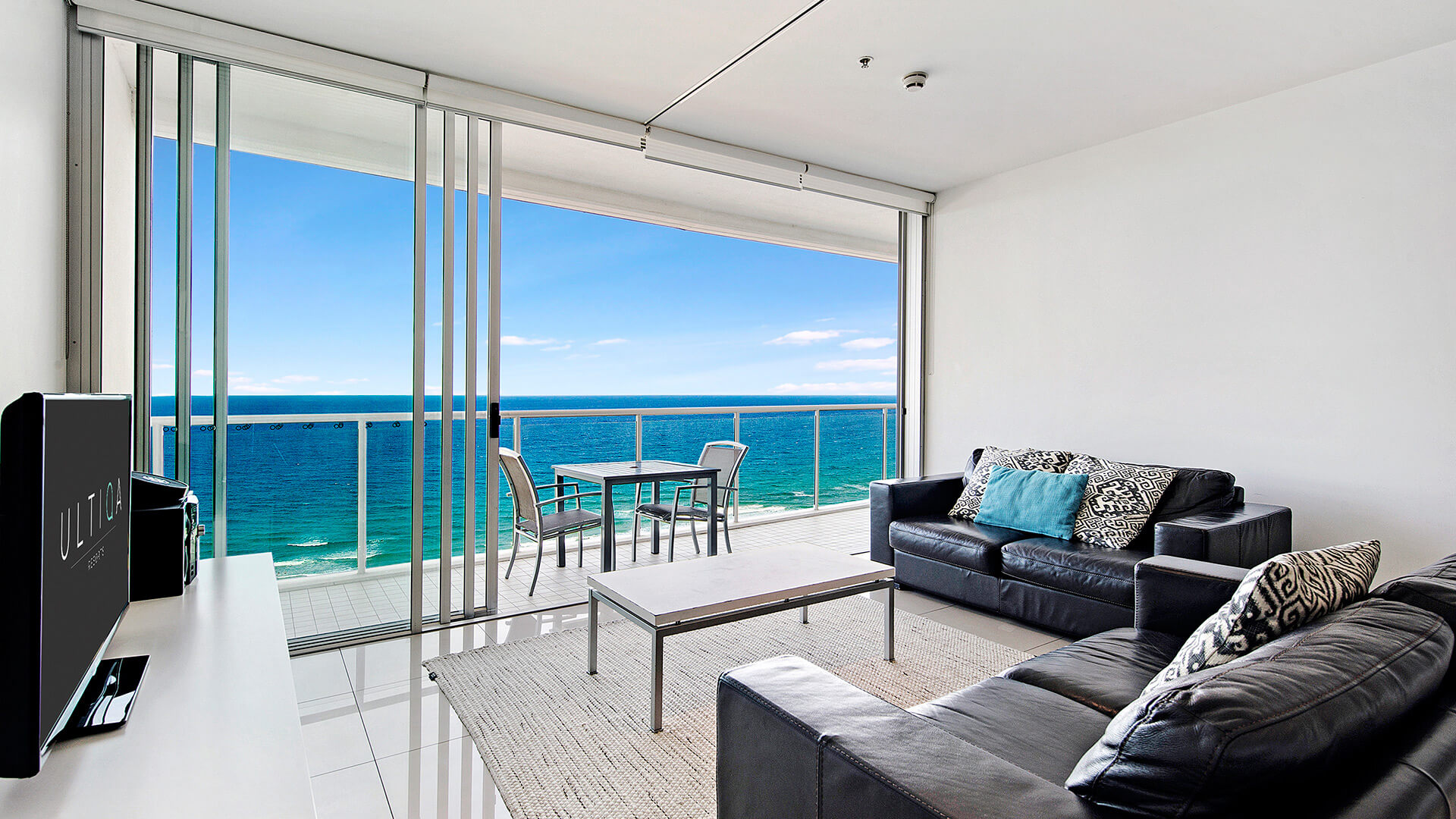 Living room with leather lounges opening onto balcony with ocean views in 2 Bedroom Ocean View Suite at ULTIQA Air on Broadbeach.
