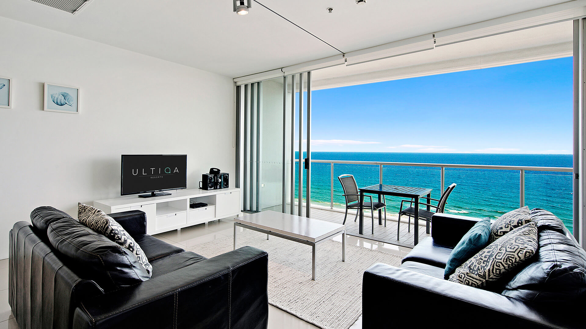 Living room with leather lounges and TV opening onto balcony with ocean views in 2 Bedroom Ocean View Suite at ULTIQA Air on Broadbeach.