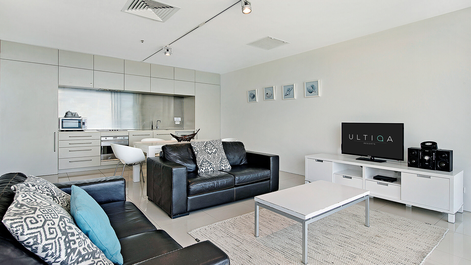Open-plan living room with leather lounges, TV, and kitchen in 2 Bedroom Ocean View Suite at ULTIQA Air on Broadbeach.