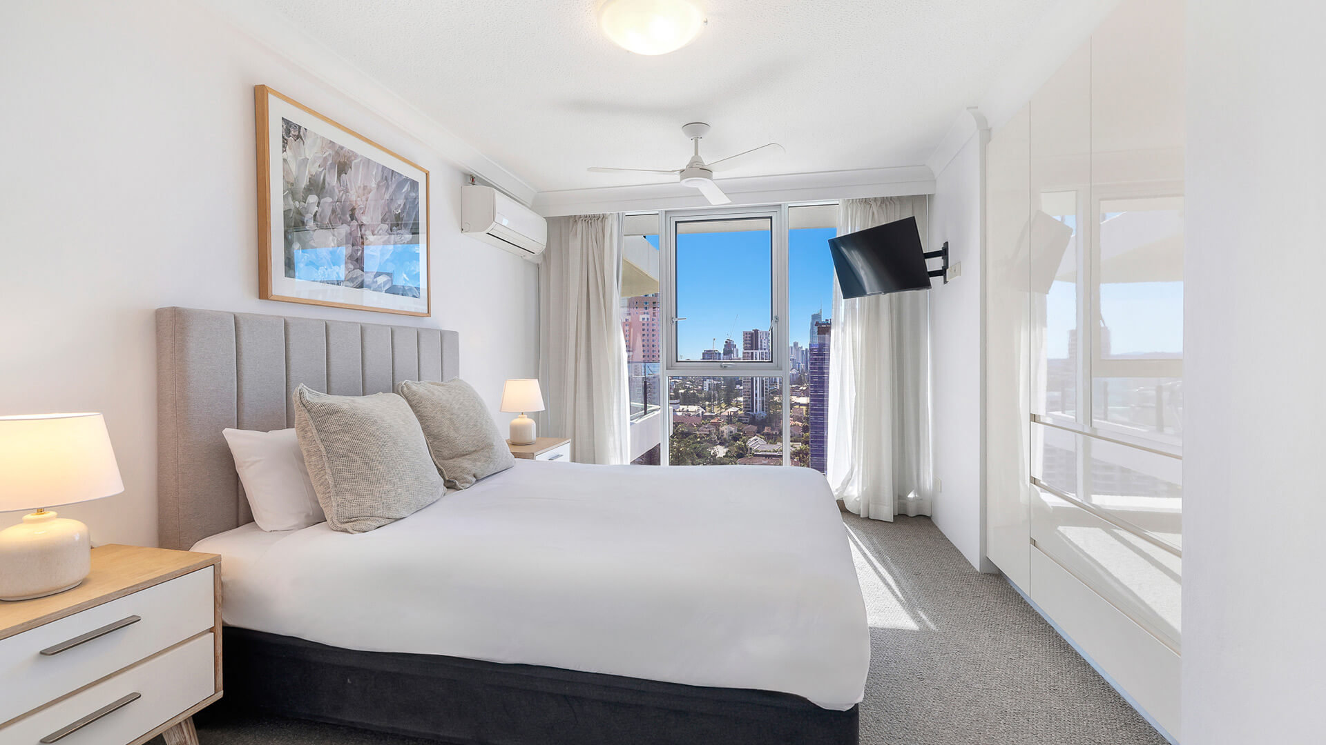 Bright bedroom in the 2 Bedroom Ocean View Apartment at ULTIQA Beach Haven featuring a king bed, built-in wardrobe, air-conditioning, and city skyline views through large windows.