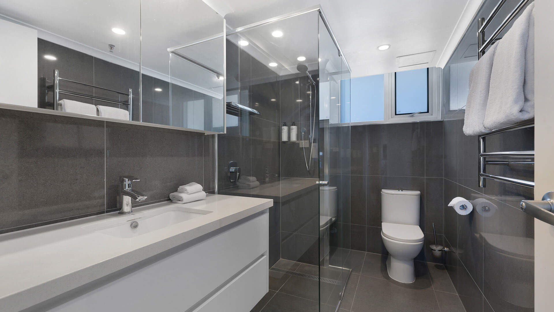 Modern featuring a glass-enclosed rainfall shower, sleek vanity, and dark floor-to-ceiling tiles.