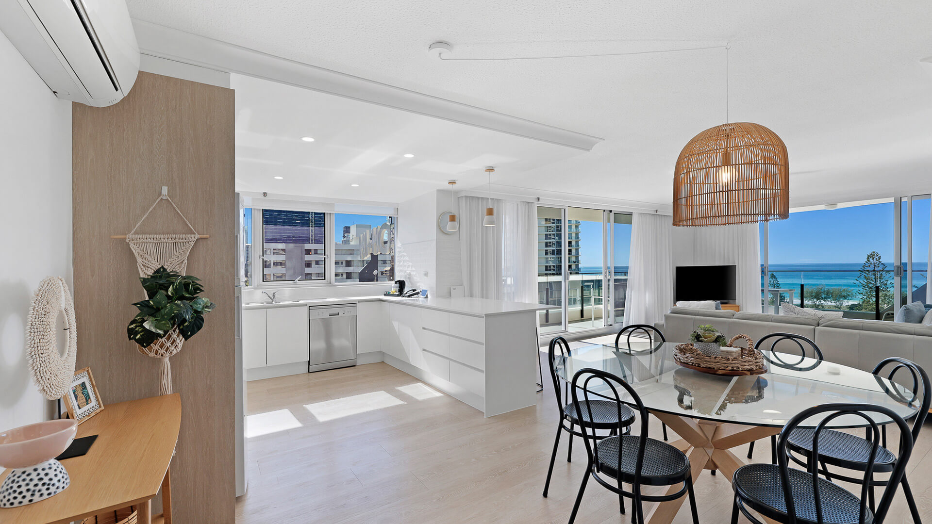 Open-plan kitchen, dining, and living featuring modern coastal décor, full kitchen, and balcony with stunning ocean views.