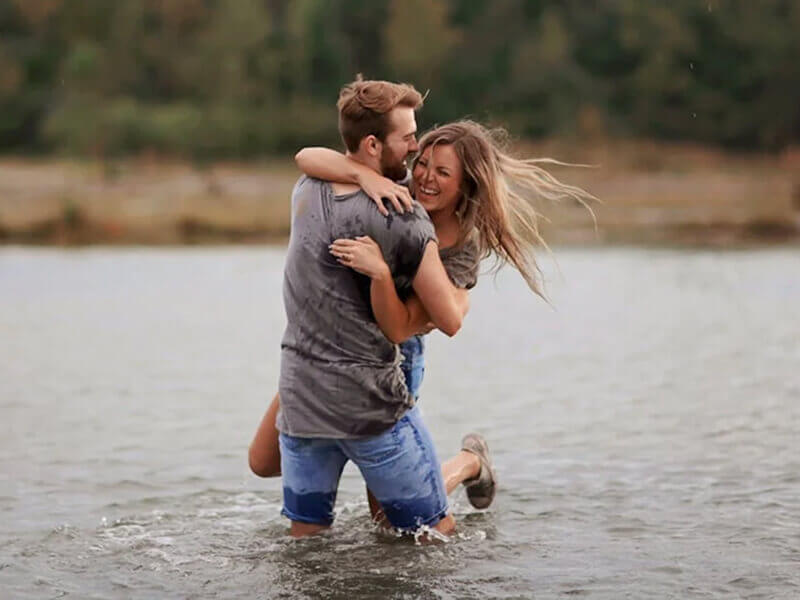 Happy couple embracing and laughing in shallow water, enjoying a carefree and joyful moment together.