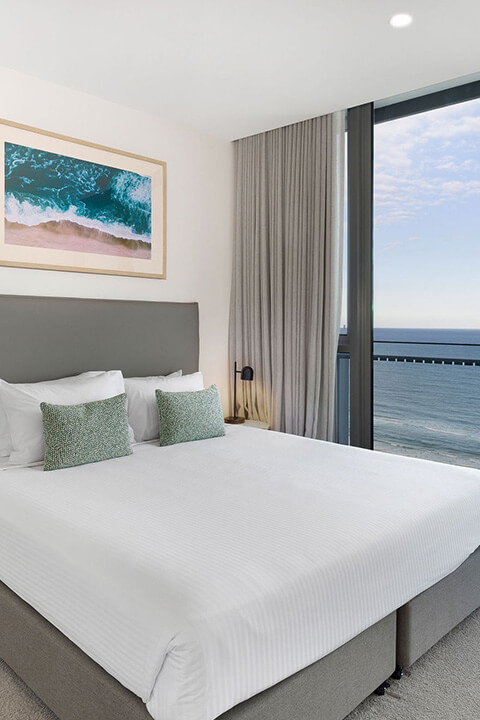 Ocean view bedroom at ULTIQA Signature at Broadbeach featuring a king bed, modern decor, and floor-to-ceiling windows overlooking the beach.