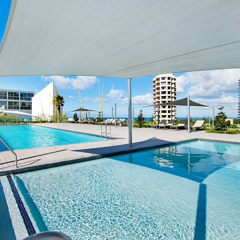 Outdoor pool deck at ULTIQA Air on Broadbeach with kids' splash pool, lap pool, loungers, and ocean views