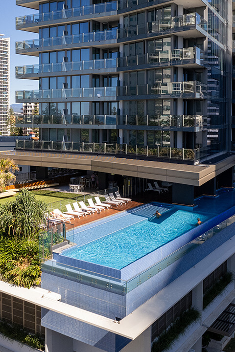 Infinity-edge pool at ULTIQA Signature at Broadbeach with sun loungers, gardens, and city views